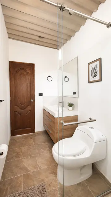 Baño con ducha en vidrio, mueble flotante en madera y puerta de madera