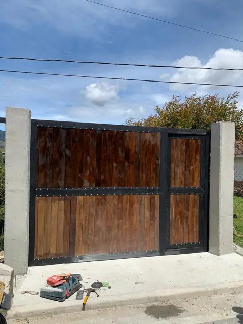 Portón en hierro negro y madera con puerta peatonal y columnas de concreto